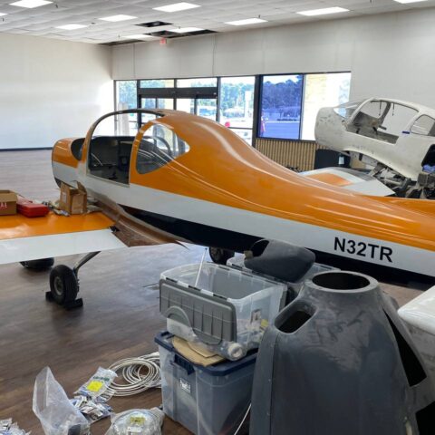A small orange and white airplane in an airport.
